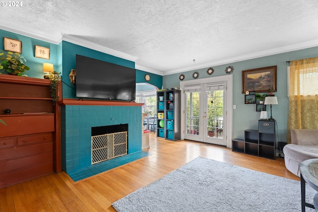 living room with a fireplace, crown molding, a textured ceiling, light hardwood / wood-style flooring, and french doors