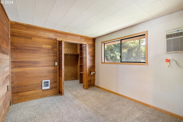 unfurnished bedroom with a closet, light colored carpet, wooden walls, and a wall unit AC