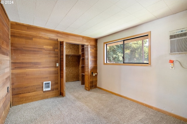 unfurnished bedroom featuring a wall mounted air conditioner, light colored carpet, a closet, and wood walls