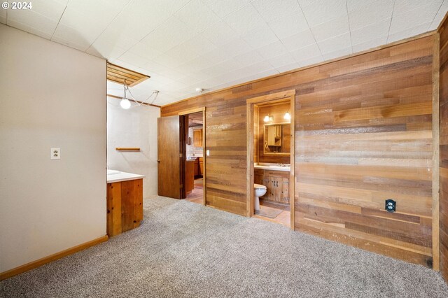 unfurnished bedroom with carpet floors, ensuite bath, and wooden walls