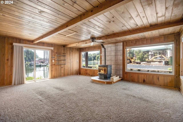 unfurnished living room featuring beam ceiling, wooden walls, carpet, a water view, and a wood stove