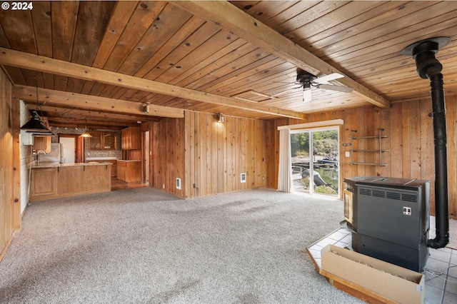 unfurnished living room featuring ceiling fan, wood walls, beamed ceiling, and a wood stove