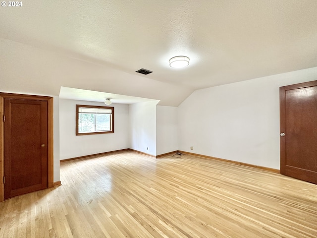 bonus room with light wood-type flooring, lofted ceiling, and a textured ceiling