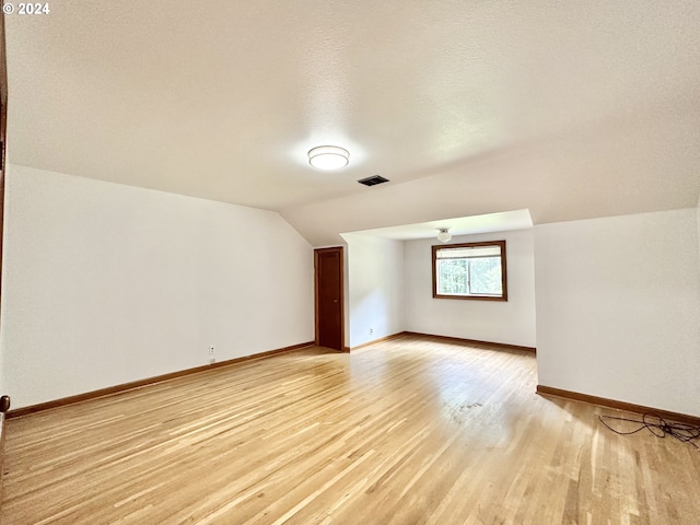 bonus room with lofted ceiling, a textured ceiling, and light hardwood / wood-style flooring