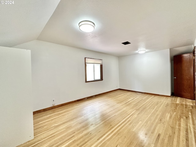 spare room with vaulted ceiling and light hardwood / wood-style flooring