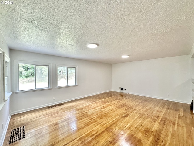 empty room with a textured ceiling and light hardwood / wood-style flooring