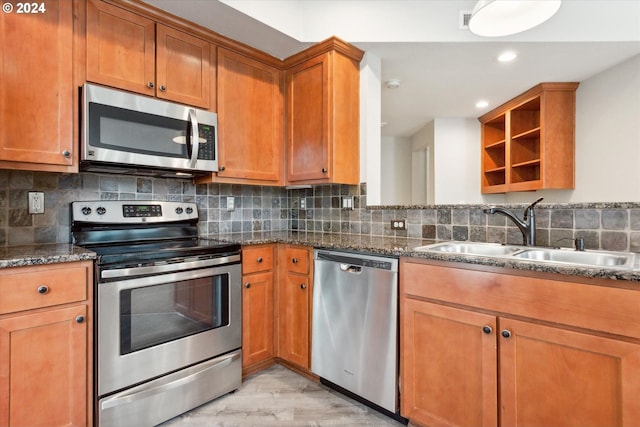 kitchen featuring sink, light hardwood / wood-style flooring, stainless steel appliances, backsplash, and dark stone countertops