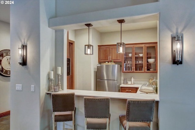 kitchen featuring kitchen peninsula, a breakfast bar area, hanging light fixtures, and stainless steel fridge