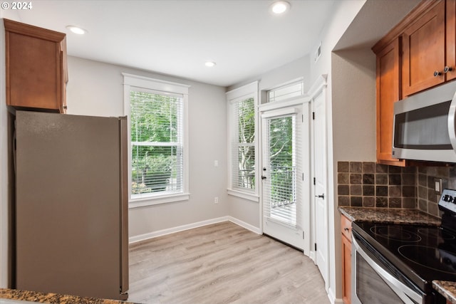 kitchen with stainless steel appliances, dark stone countertops, light hardwood / wood-style floors, and plenty of natural light