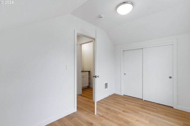 unfurnished bedroom featuring light hardwood / wood-style flooring, a closet, and vaulted ceiling