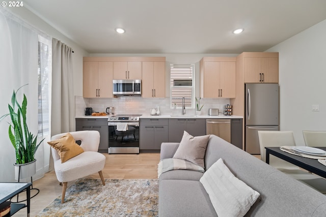 kitchen with light brown cabinets, sink, tasteful backsplash, stainless steel appliances, and light hardwood / wood-style floors