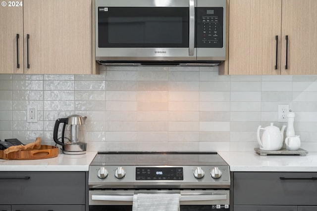 kitchen with light stone countertops, backsplash, light brown cabinets, and appliances with stainless steel finishes