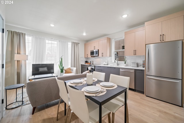 kitchen featuring light brown cabinets, gray cabinetry, appliances with stainless steel finishes, light wood-type flooring, and decorative backsplash