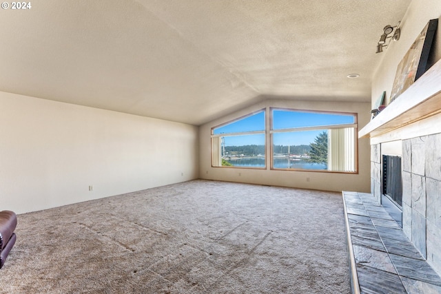 unfurnished living room with a water view, a fireplace, a textured ceiling, lofted ceiling, and carpet