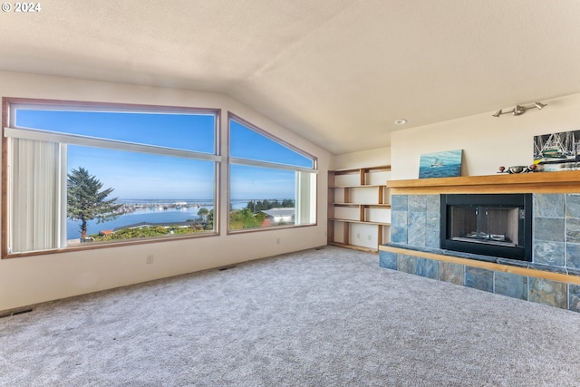 unfurnished living room featuring a textured ceiling, lofted ceiling, a tiled fireplace, carpet floors, and a water view