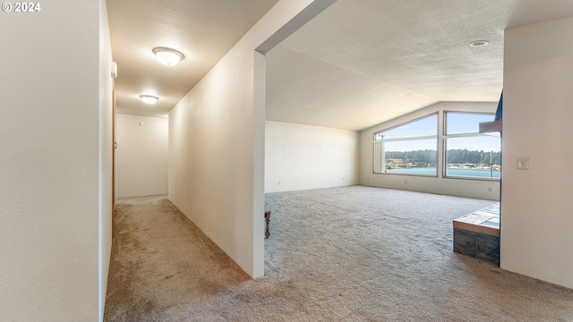 additional living space with light colored carpet, a textured ceiling, lofted ceiling, and a water view