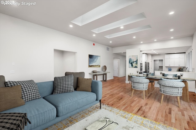 living room with a skylight, sink, and light hardwood / wood-style flooring