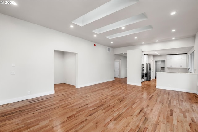 unfurnished living room with sink, light hardwood / wood-style floors, and a skylight