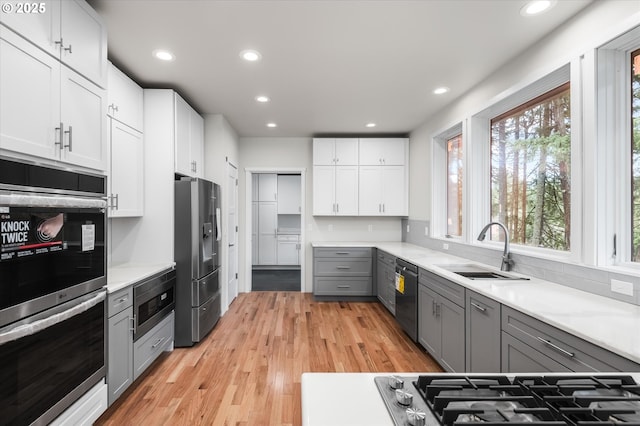 kitchen with sink, gray cabinetry, white cabinetry, appliances with stainless steel finishes, and light hardwood / wood-style floors