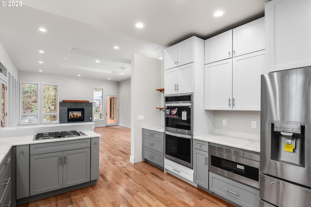 kitchen featuring gray cabinets, a multi sided fireplace, appliances with stainless steel finishes, white cabinets, and light hardwood / wood-style floors