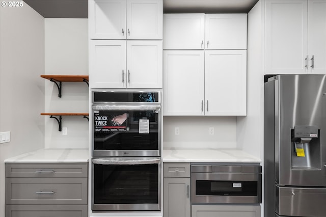 kitchen featuring white cabinetry, appliances with stainless steel finishes, light stone counters, and gray cabinetry