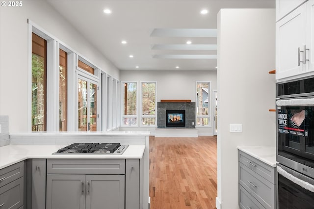 kitchen featuring light hardwood / wood-style flooring, appliances with stainless steel finishes, gray cabinetry, a fireplace, and white cabinets