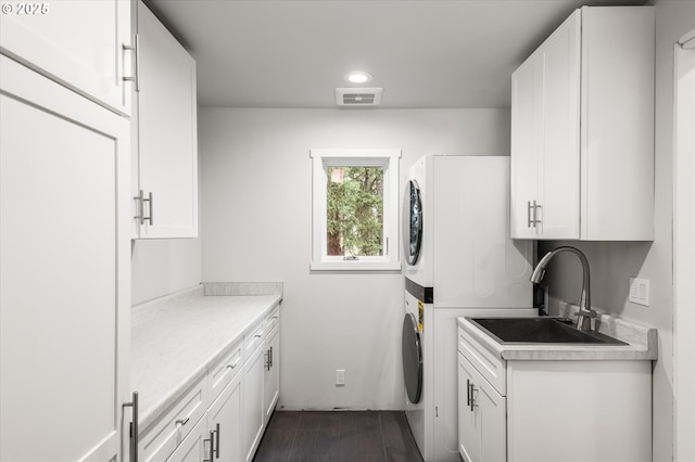 clothes washing area with cabinets, stacked washer and dryer, and sink