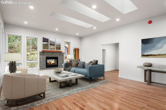 living room with a skylight, a tiled fireplace, and light hardwood / wood-style flooring