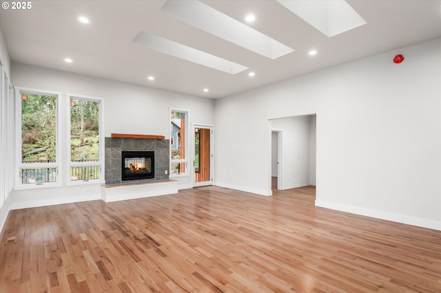 unfurnished living room featuring a tiled fireplace, a skylight, and light hardwood / wood-style floors