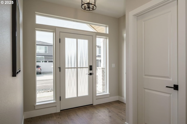 doorway with baseboards, an inviting chandelier, and wood finished floors