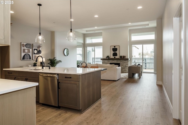 kitchen featuring a fireplace, a sink, light countertops, light wood-style floors, and dishwasher