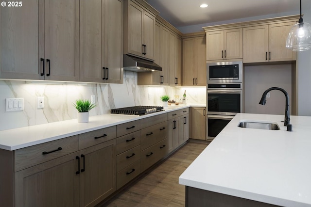 kitchen featuring under cabinet range hood, built in microwave, decorative backsplash, gas stovetop, and a sink