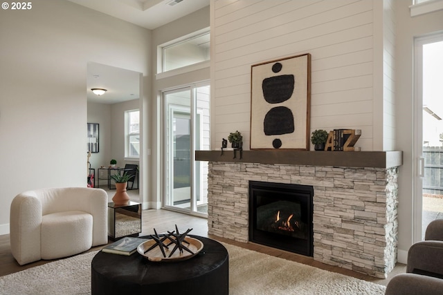 living room featuring wood finished floors, visible vents, baseboards, a fireplace, and a towering ceiling