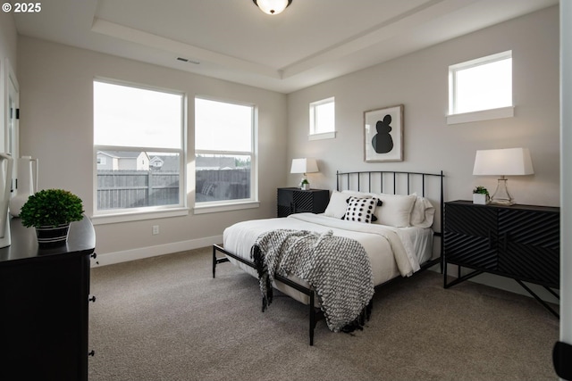 carpeted bedroom featuring a tray ceiling, baseboards, and visible vents