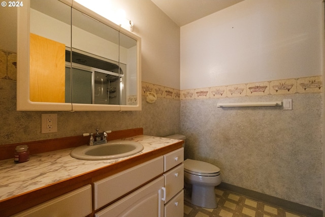 bathroom with a stall shower, toilet, a wainscoted wall, tile patterned floors, and vanity