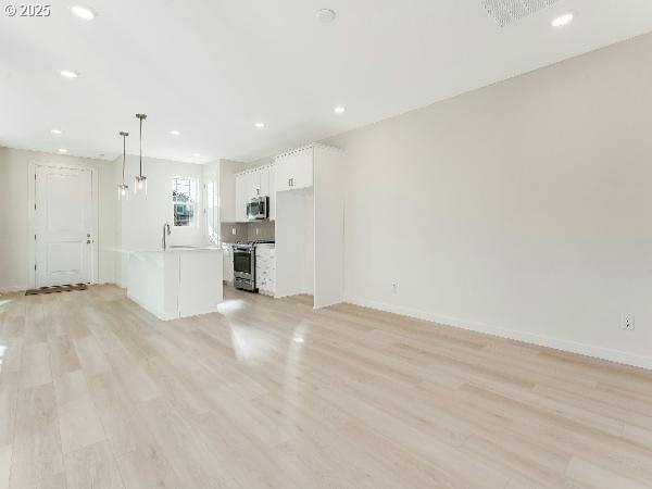 unfurnished living room featuring light wood-style floors, baseboards, a sink, and recessed lighting