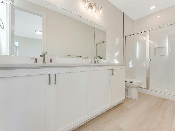 bathroom with double vanity, toilet, a sink, a shower stall, and wood finished floors