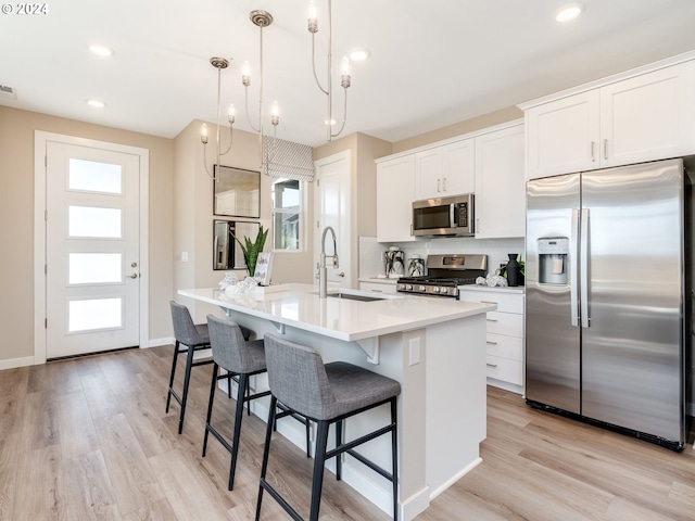 kitchen featuring appliances with stainless steel finishes, sink, pendant lighting, white cabinetry, and an island with sink