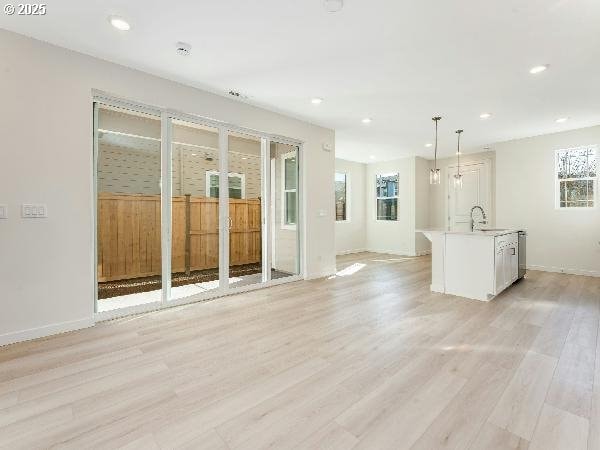 unfurnished living room featuring light wood-type flooring, baseboards, a sink, and recessed lighting