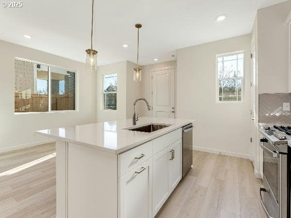 kitchen with decorative light fixtures, stainless steel appliances, white cabinetry, light countertops, and a center island with sink