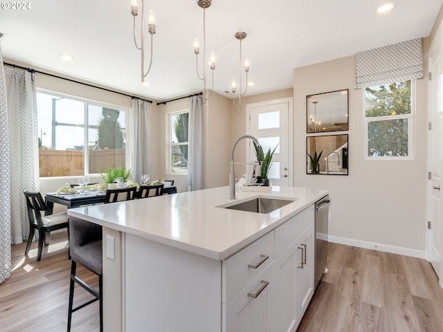 kitchen featuring pendant lighting, a center island with sink, white cabinets, stainless steel dishwasher, and light wood-type flooring