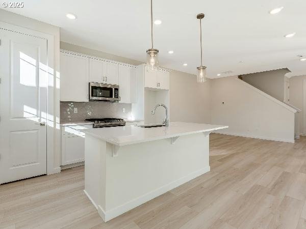 kitchen featuring a kitchen island with sink, a sink, light countertops, stainless steel microwave, and decorative light fixtures