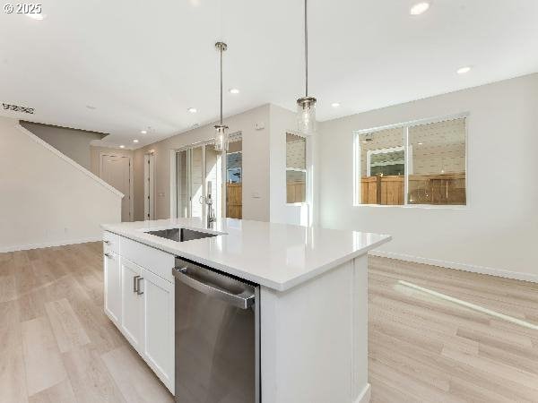 kitchen with pendant lighting, light countertops, stainless steel dishwasher, a kitchen island with sink, and white cabinets