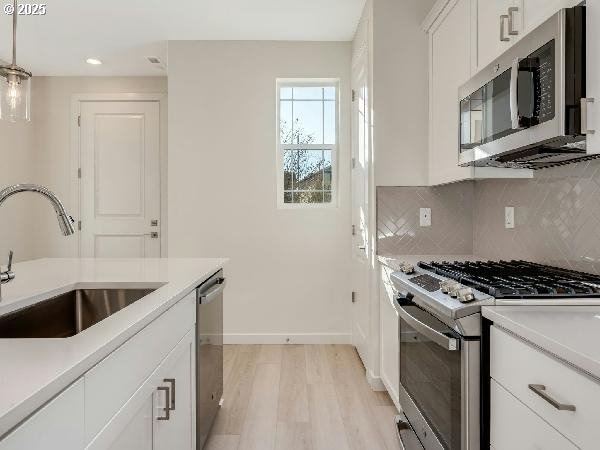 kitchen featuring stainless steel appliances, a sink, white cabinetry, hanging light fixtures, and light countertops