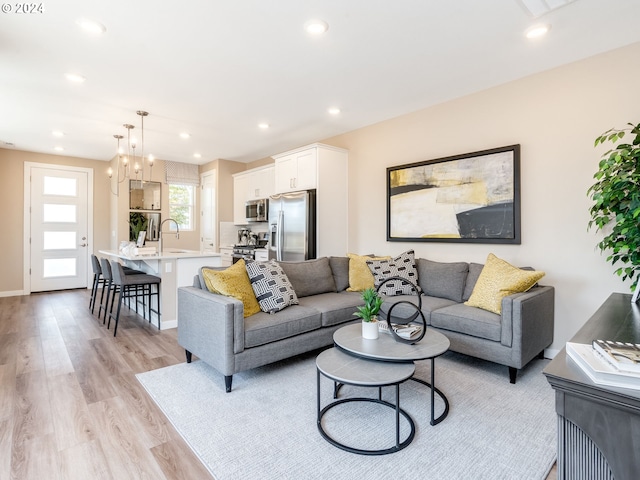 living room featuring light wood-type flooring, an inviting chandelier, and sink