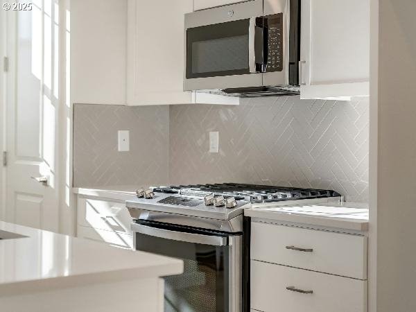 kitchen with stainless steel appliances, light countertops, white cabinetry, and backsplash