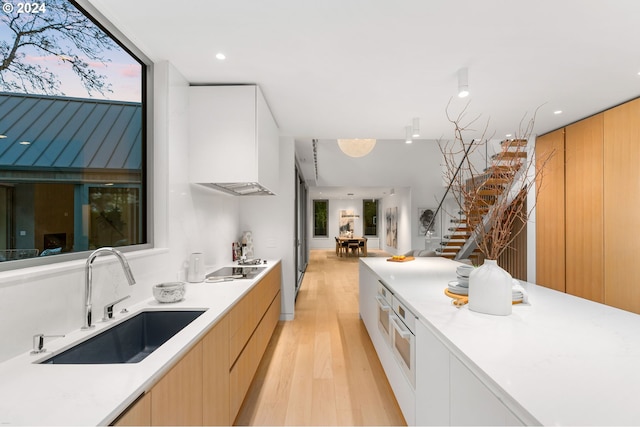 kitchen with light wood-type flooring, oven, electric stovetop, sink, and white cabinetry