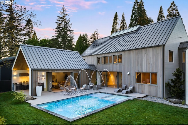 back house at dusk featuring a yard, a patio area, and pool water feature