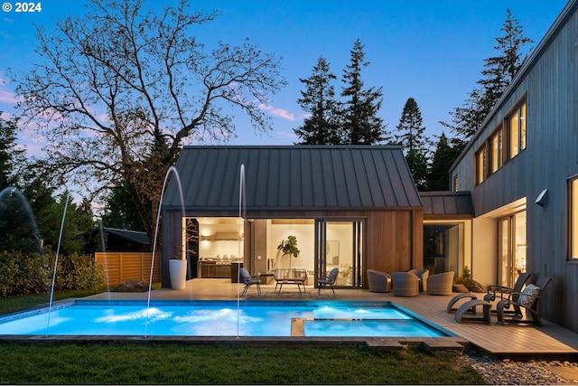 back house at dusk with pool water feature and a swimming pool side deck