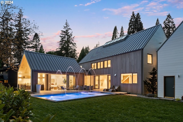 back house at dusk featuring a patio and a lawn